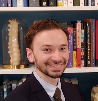 Photo of Emilio Valadez smiling and standing in front of a bookcase